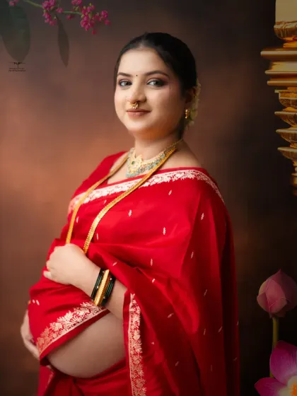 A simple yet stunning portrait of the mother-to-be. Her gentle smile and the rich red of her saree create a beautiful, classic image against the warm, textured backdrop.