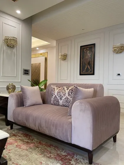 The pastel pink sofa with channel tufting adds a touch of softness and modern elegance. The classic wainscoting on the walls provides a sophisticated, architectural backdrop.
