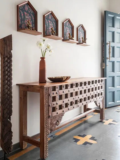 This gorgeous teak console, likely repurposed from an old door, is a conversation starter in the foyer. Above it, custom-made shelves house antique brass sculptures of musicians, adding to the home's authentic, vintage charm.