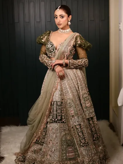 A full view of this elegant bridal look. The simple, floral-accented bun is the perfect hairstyle to pair with her unique olive green lehenga with statement puff sleeves.