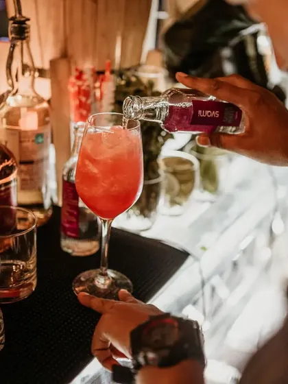 A close up of a cocktail being crafted. Our mixologist adds a final touch to a vibrant red drink, showcasing the care that goes into every single order.