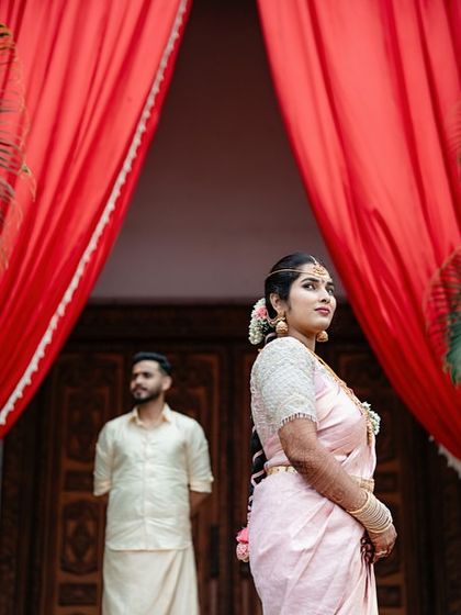 A creative portrait of a couple, with the bride in the foreground and the groom in the background, framed by dramatic red curtains.