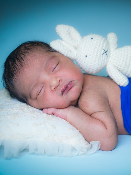 A sleeping newborn boy with a knitted bunny toy. The simple, solid blue background makes the baby and his little friend stand out.