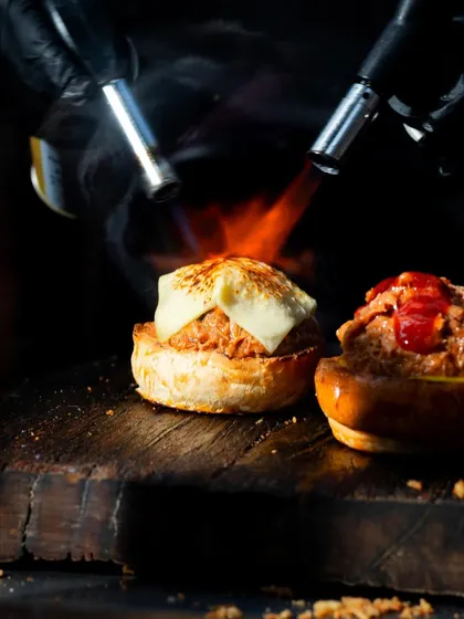 A wider view of the blowtorching process, showing the chef's technique and the delicious result on two bagels.