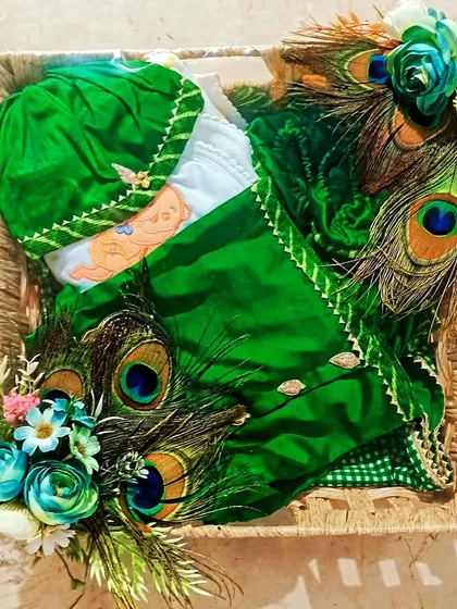 A unique trousseau packing featuring a green baby outfit decorated with real peacock feathers for a touch of tradition.