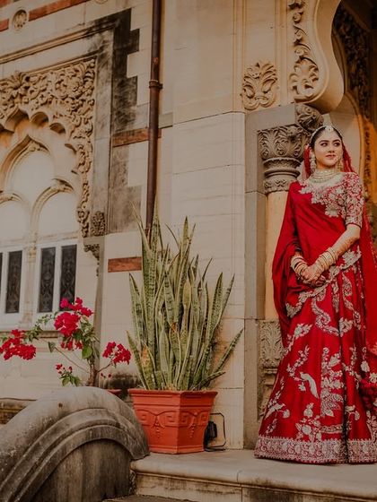 A beautiful solo portrait of the bride in her red lehenga against the intricate architecture of the palace.