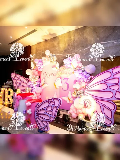 Another perspective of Nyra's butterfly birthday stage, highlighting the large marquee letters and the beautiful arrangement of props and balloons.