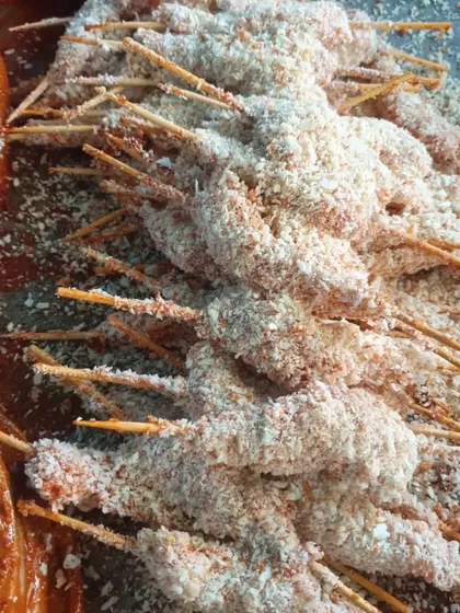 Chicken lollipops coated in a breadcrumb mixture, ready for deep frying.