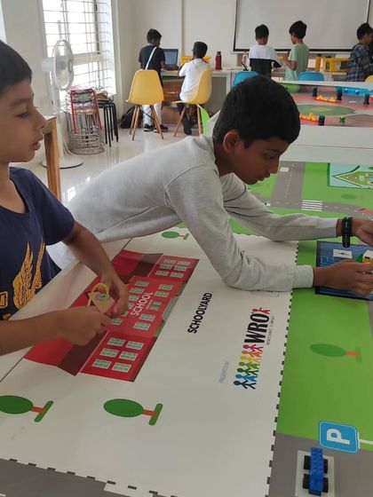 Two students collaborate on the competition mat, strategizing their robot's path to efficiently complete the autonomous school bus challenge.