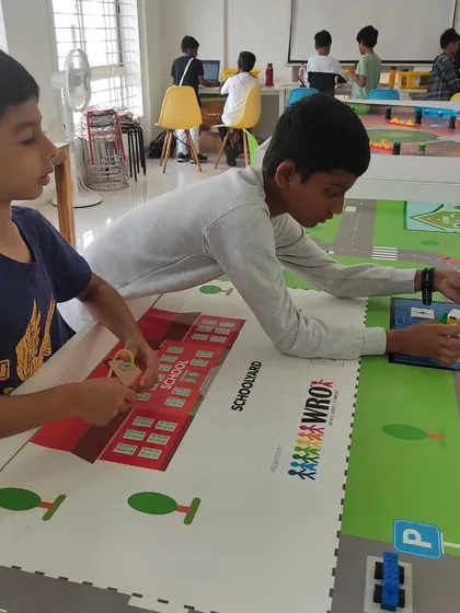 Two students collaborate on the competition mat, strategizing their robot's path to efficiently complete the autonomous school bus challenge.