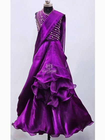 A modern ruffled gown in a rich purple organza. The sleeveless bodice has simple pearl work, and the skirt has dramatic ruffles.