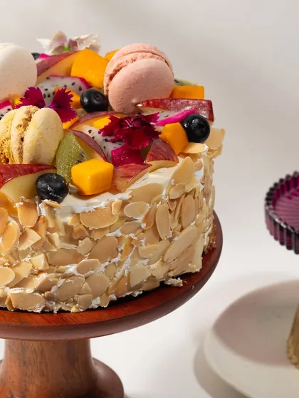 A side view of my Almond & Fruit Cake, showing the crunchy toasted almonds covering the sides and the abundance of fresh fruit and macarons on top.