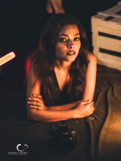 A moody and atmospheric portrait, with the subject holding a camera. The low light and her intense gaze create a story about the person behind the lens.