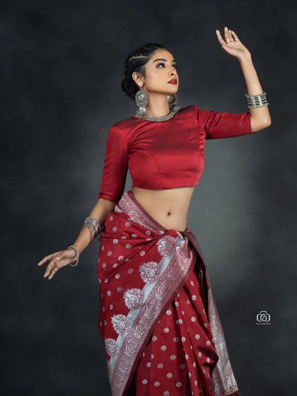 A graceful pose in a red fusion saree look. The lighting captures the rich color of the fabric and the shine of the silver jewelry, creating a striking contrast.