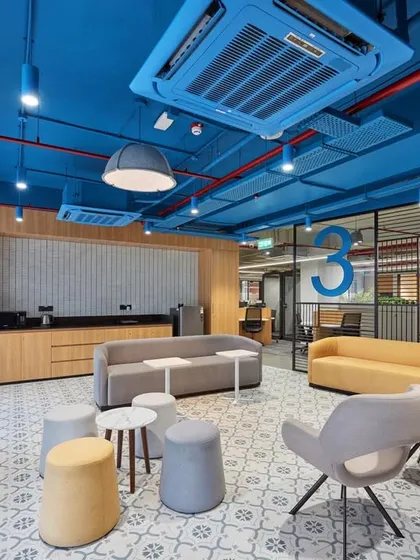 A spacious lift lobby lounge with a bright blue ceiling and a variety of seating options. The patterned floor adds a classic touch to the modern design.