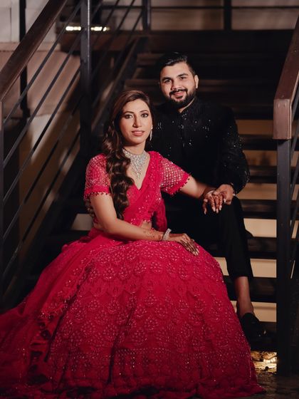 The couple poses for a portrait on a staircase. Their elegant red and black outfits and the classic setting create a timeless and sophisticated image.