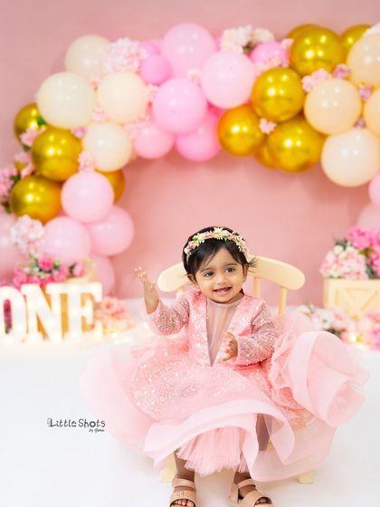 A happy wave from the birthday girl! This shot captures her personality and the festive atmosphere of her pretty pink first birthday photoshoot.