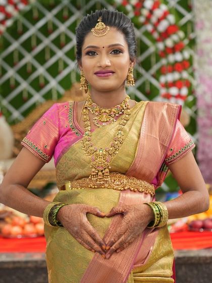 Our beautiful mom-to-be, Malini, making a heart with her hands. She is glowing in a full temple jewellery set, including a choker, haram, and vaddanam.