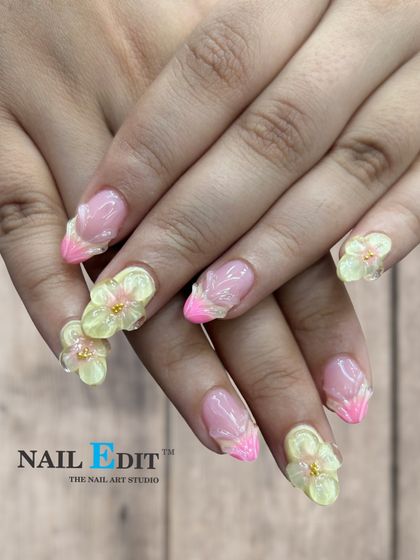 We can create 3D floral designs that seem to bloom right off your nails. This set features translucent yellow sculpted flowers on a French manicure base with bright pink tips, perfect for a vibrant, spring-inspired style.