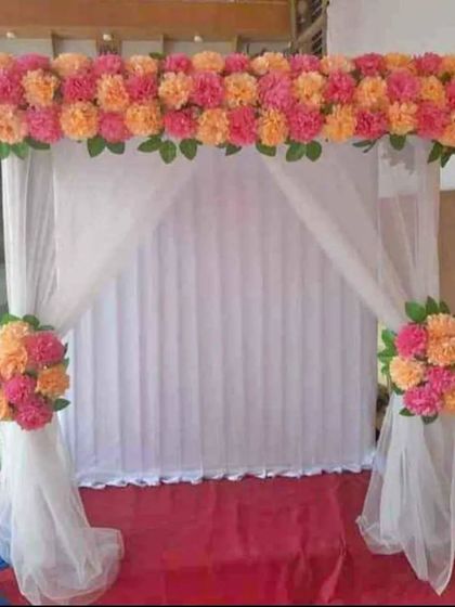 A simple and budget-friendly option for a traditional look. This setup uses a white curtain backdrop framed with artificial marigold bunches in shades of pink and orange, offering a bright and festive feel.