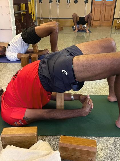 A close-up of Rohan Bopanna in a supported Bridge Pose. The use of blocks allows for a longer, more passive hold, facilitating deep release in the quadriceps and psoas muscles, which often become tight in athletes.
