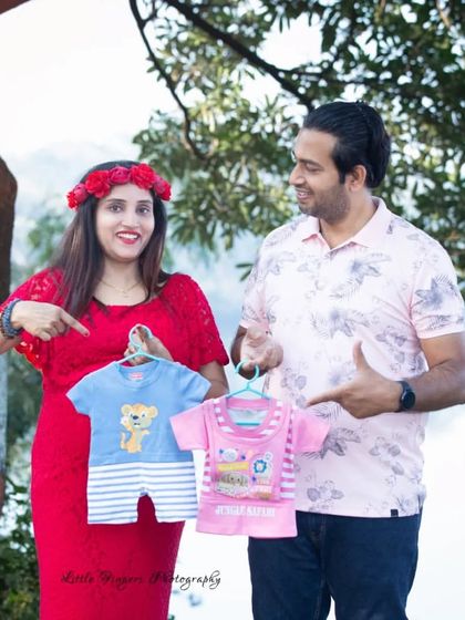 A fun and colorful gender reveal moment during a maternity shoot, with the couple holding up tiny pink and blue outfits.