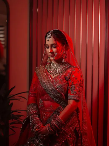 A stunning bridal portrait using dramatic red lighting to create a bold, cinematic feel. This shot highlights the bride's serene expression and the intricate details of her red lehenga and jewelry.