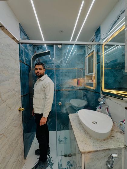 Proudly standing in a completed bathroom that showcases a mix of blue and white marble tiles, a glass shower enclosure, and modern fixtures.