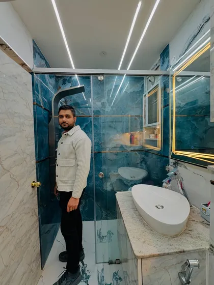 Proudly standing in a completed bathroom that showcases a mix of blue and white marble tiles, a glass shower enclosure, and modern fixtures.