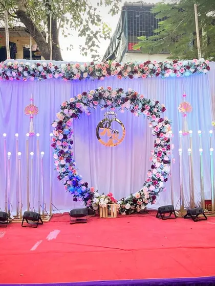 An outdoor engagement stage setup with a floral ring. The white and patterned backdrops are complemented by a red carpet and uplighting.