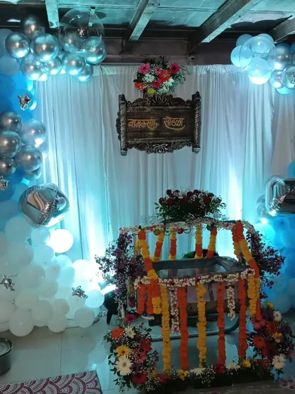 A traditional naming ceremony setup with a beautifully decorated wooden cradle (palna) as the centerpiece, surrounded by blue and silver balloon arrangements.