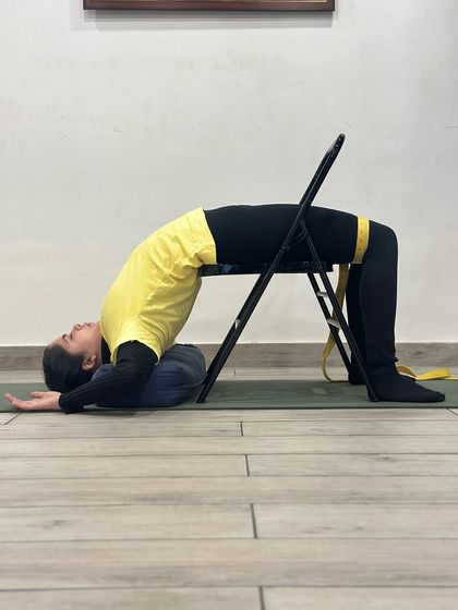 This is another variation of Chatushpadasana, using a chair and a belt around the thighs. The belt provides resistance, helping to activate the outer hip muscles and maintain the alignment of the knees, making the pose more stable and effective.