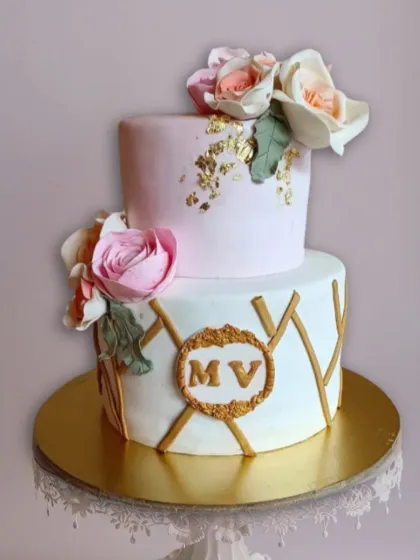 A chic two-tier cake with a modern geometric gold pattern on the bottom tier and soft pink sugar flowers.