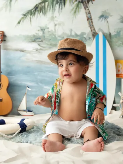 A sweet portrait of a toddler in a Hawaiian shirt and hat, enjoying his beach-themed sitter session.