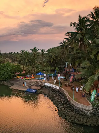 A duplicate of image 57, showing a beautiful winter sunset over a coastal inlet in Udupi, with palm trees and a small recreational area.