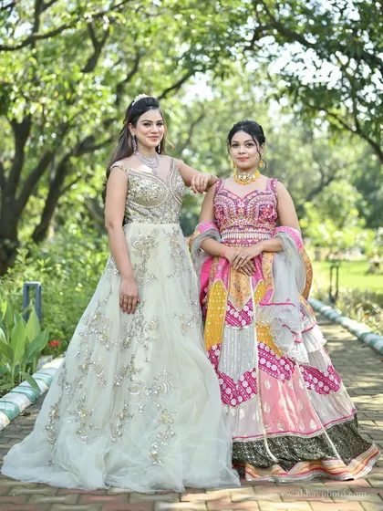 A model in a pastel green gown posing with another in a vibrant pink and yellow patchwork lehenga, showing how different styles can complement each other.