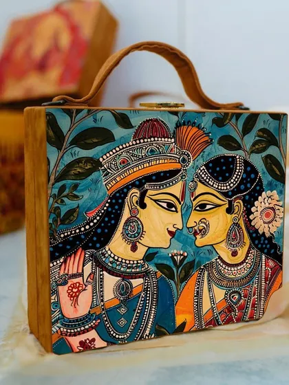 This bag is adorned with a traditional painting of Radha and Krishna, making it a piece of wearable art. The rich colors and intricate details are printed on matte satin, framed by a tan suede body.