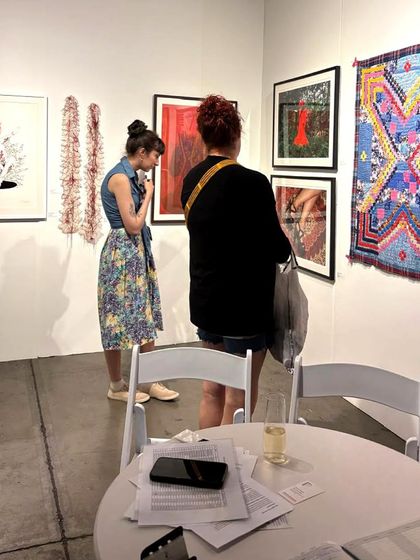 Visitors at the Seattle Art Fair examining a vibrant textile piece by the Siddi Quilters and framed works by other artists. This shows the diverse range of art we present, from traditional crafts to contemporary photography.