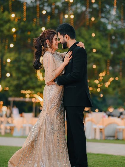 A romantic evening shot of a couple embracing in a garden decorated with fairy lights. The warm glow creates a magical and celebratory atmosphere for this engagement shoot.