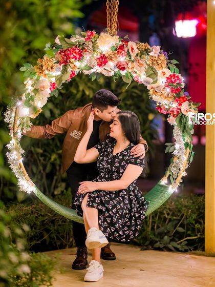 A sweet kiss on the forehead captured on the floral swing, with the evening lights creating a warm and romantic glow.