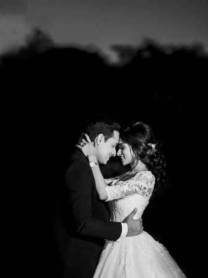 A romantic black and white portrait of the couple in an embrace. The dark, minimalist background makes their connection the central story.
