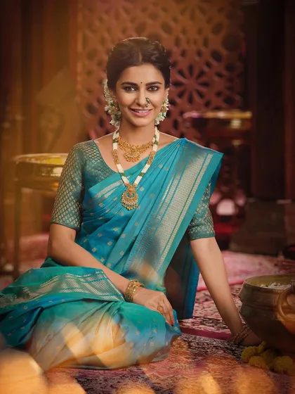 A full view of the seated model, showing the graceful drape of the traditional saree and the complete set of gold jewelry, perfect for a Maharashtrian bride.