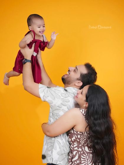 Pure happiness as a father lifts his giggling baby into the air. The bright, solid-colored background makes this joyful moment pop.