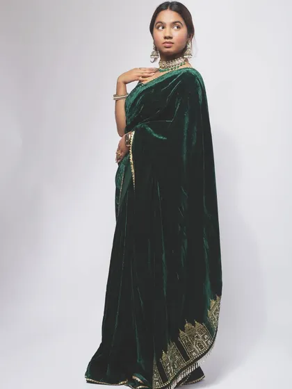 A full-length shot of a luxurious green velvet saree. This image is designed for e-commerce, showing the complete look, the fall of the fabric, and the intricate border design.