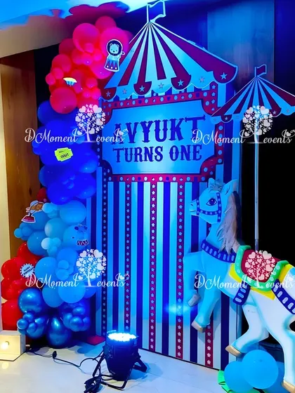 A photo booth area at the carnival party, featuring a carousel horse prop, a large "1" marquee light, and a backdrop designed to look like a circus tent.