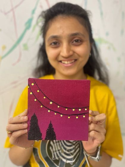 A happy artist holds up the charming mini-canvas she painted, proving that great art can come in small packages.