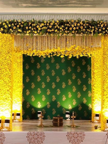 A yellow floral mandap set against a traditional green printed backdrop, designed for a heritage home wedding in Kerala.