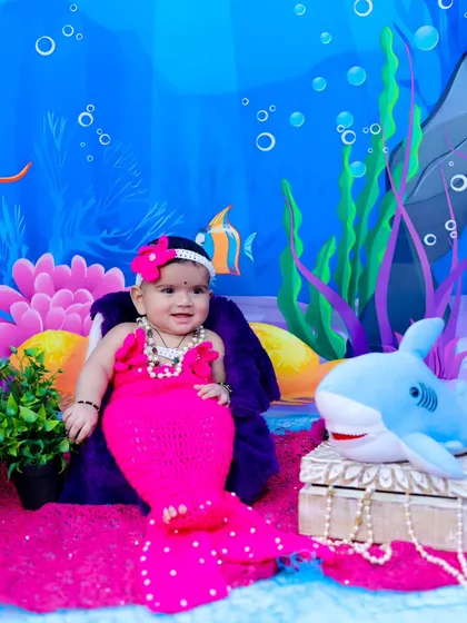 Another adorable little mermaid, this time in a bright pink outfit, smiling for her underwater portrait.