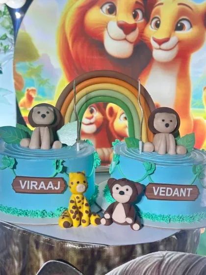 Twin cakes for Viraaj and Vedant! This Lion King inspired setup features two separate cakes connected by a fondant rainbow, with cute animal figures.