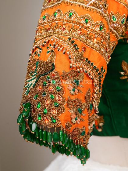 This blouse is a celebration of vibrant color and artistry. I used a rich green raw silk base and contrasted it with bright orange sleeves, which feature incredibly detailed peacock embroidery using zardozi, stones, and beadwork.